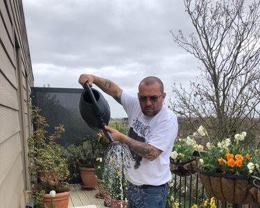 Chris Collins is watering various plant pots and trays of seeds on his balcony.
