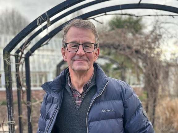 A man wearing glasses standing under a garden archway