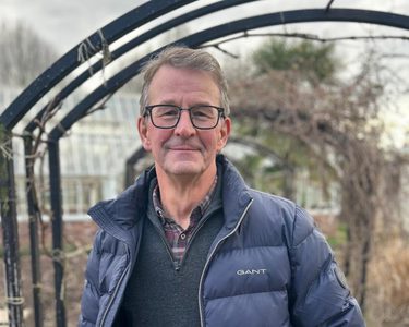 A man wearing glasses standing under a garden archway